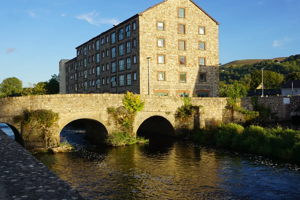 The stone Old Bridge over the River Suir in Clonmel, with a restored mill building in evening sun