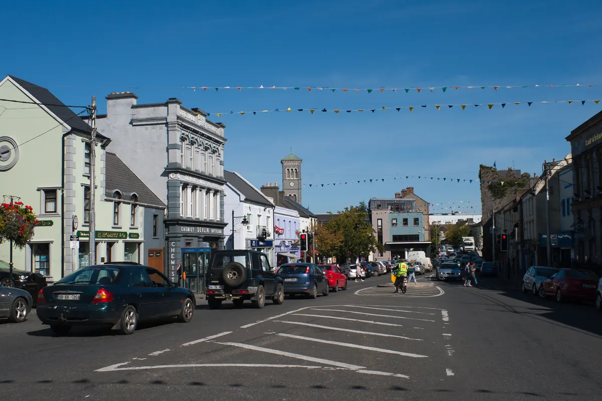 Liberty Square in Thurles on a sunny day, with shopfronts, bunting and the cathedral bell tower in the distance